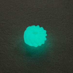 May include: A teal-coloured, glowing object with a textured, rounded form. The object emits a bright, soft light against a dark background. The design appears to be a decorative element or a small, illuminated sculpture.