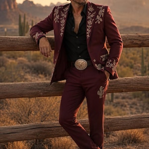 May include: A burgundy suit featuring gold floral embroidery on the lapels and cuffs, paired with a black shirt, a large circular gold belt buckle, a black cowboy hat, and black boots. The trousers are adorned with small gold cactus embroidery.