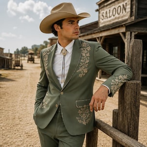 May include: A sage green blazer featuring intricate gold floral embroidery on the lapels, pockets, and sleeves. The blazer is worn over a crisp white button-down shirt with a bolo tie, paired with a tan cowboy hat in a dusty outdoor setting.
