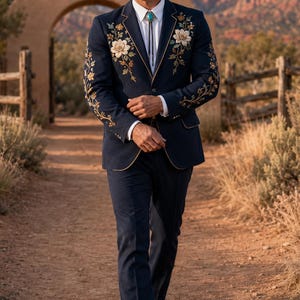 Könnte beinhalten: Ein marineblauer Anzug mit passender Hose, verziert mit floralen Stickereien auf Brust und Ärmeln, kombiniert mit einem weißen Hemd, einer türkisfarbenen Bolo-Krawatte, einem hellen Cowboyhut und braunen Lederschuhen.