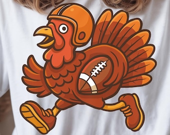 Könnte beinhalten: Ein elfenbeinfarbenes T-Shirt mit einer grafischen Illustration eines braunen Truthahns, der einen orangefarbenen Football-Helm und Laufschuhe trägt und einen braun-weißen Football unter dem Flügel hält. Der Truthahn hat orange und braune Federn.