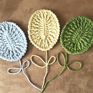 May include: Three crocheted flower shapes in blue, yellow, and green. The flowers are connected by their stems, which are made of the same yarn.