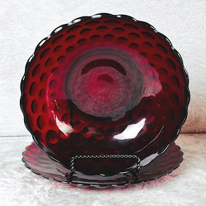Puede incluir: Un par de cuencos de vidrio rojo intenso con un patrón circular de hoyuelos en la superficie interior. Los cuencos tienen un borde festoneado y un diseño radial de rayos de sol en la base, hechos de vidrio color rubí translúcido.