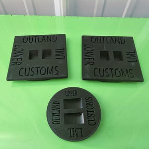 Pode incluir: Três peças personalizadas verde escuro. Duas são quadradas com o texto "OUTLAND", "LOWER", "CUSTOMS" e "LML". A terceira peça é redonda com o texto "OUTLAND", "UPPER", "CUSTOMS" e "LML".