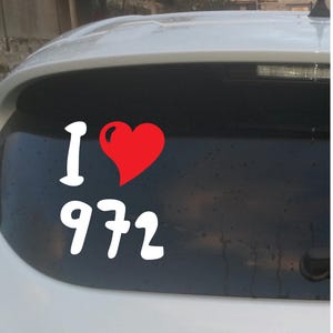 Puede incluir: Adhesivo de vinilo blanco con el texto "I ❤️ 972" en un estilo manuscrito. El corazón es rojo. El adhesivo está pegado en la ventana trasera de un coche blanco.