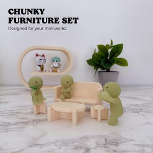 May include: A miniature furniture set featuring a beige sofa, a matching oval coffee table, and two small stools. Three small, smooth, olive-green humanoid figurines are positioned around the furniture. Text reads CHUNKY FURNITURE SET.