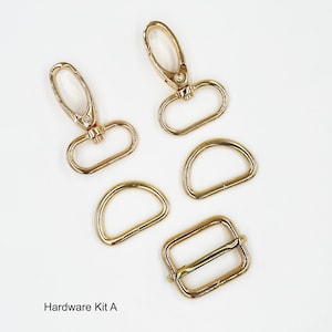 May include: A set of gold-toned metal hardware including two lobster claw clasps, two D-rings, and one rectangular slider buckle. The items are arranged on a plain background with the text Hardware Kit A printed in the bottom left corner.