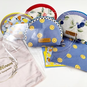 May include: A collection of handmade fabric pouches with various patterns, including lemons, blueberries, and smiley faces. The pouches are in shades of blue, yellow, and white, with a clear acrylic template and a pink cloth with the text "Melbloom Acrylic Templates".