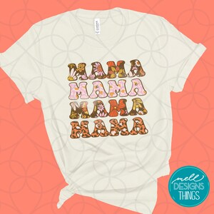 May include: Cream-colored t-shirt with the word "MAMA" repeated four times in a retro font. Each word is decorated with floral and animal print patterns in shades of brown, pink, orange, and yellow. The shirt has rolled-up sleeves.