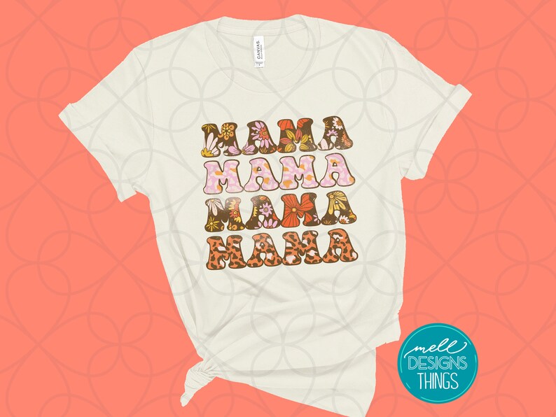 May include: Cream-colored t-shirt with the word "MAMA" repeated four times in a retro font. Each word is decorated with floral and animal print patterns in shades of brown, pink, orange, and yellow. The shirt has rolled-up sleeves.