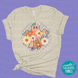 May include: A beige t-shirt with a retro-style ghost design. The ghost is made up of colorful flowers and has a checkered pattern behind it.