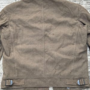 Puede incluir: Chaqueta marr&oacute;n con cuello con solapas y dos correas ajustables en la cintura con hebillas met&aacute;licas. La parte trasera de la chaqueta tiene una costura vertical en el centro y cierre de bot&oacute;n en la parte inferior.