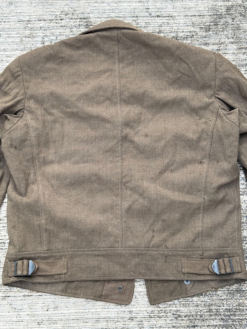 Puede incluir: Chaqueta marr&oacute;n con cuello con solapas y dos correas ajustables en la cintura con hebillas met&aacute;licas. La parte trasera de la chaqueta tiene una costura vertical en el centro y cierre de bot&oacute;n en la parte inferior.