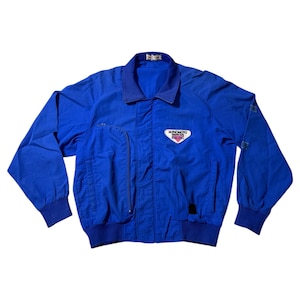 May include: A bright blue jacket with a collared neckline and long sleeves. The jacket has a zippered front, multiple pockets, and a small logo patch on the chest. The cuffs and collar are a darker shade of blue.