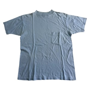 Könnte beinhalten: Hellblaues T-Shirt mit einer Tasche auf der linken Brust. Das Shirt hat kurze Ärmel und einen gerippten Rundhalsausschnitt. Der Stoff scheint ein weiches, leichtes Material zu sein.