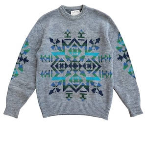 May include: A gray sweater with a geometric pattern in shades of blue and green. The pattern is centered on the chest and repeated on the sleeves. The sweater has a crew neck and ribbed cuffs.