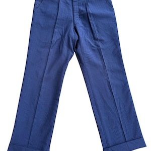 May include: Navy blue trousers with a subtle vertical stripe pattern. The pants feature a pleated front, side pockets, and cuffed hems. The waistband has a striped lining. These classic trousers are suitable for various occasions.