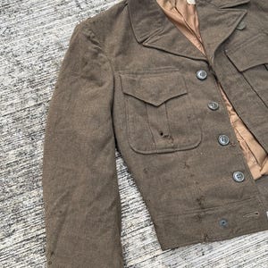 Puede incluir: Chaqueta vintage de lana marr&oacute;n con un dise&ntilde;o cl&aacute;sico. La chaqueta presenta un cuello con solapas, dos bolsillos delanteros y cierres de botones. El forro interior es de color marr&oacute;n claro. La chaqueta muestra signos de desgaste.