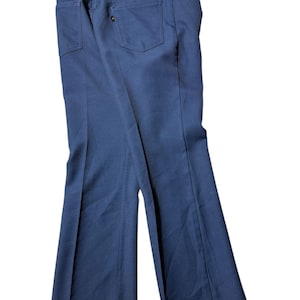 Peut inclure: Pantalon bleu foncé avec une coupe évasée. Le pantalon a deux poches arrière et une fermeture à bouton et fermeture éclair. Le tissu semble être un matériau de poids moyen, adapté aux tenues décontractées.
