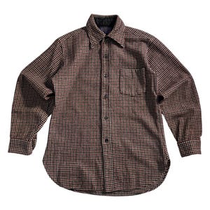 Peut inclure: Chemise à manches longues à carreaux marron, noir et rouge. Elle présente une poche poitrine et un col classique. Le tissu semble être de poids moyen, avec une coupe droite et des boutons noirs.