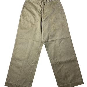 May include: Wide-leg khaki trousers. The trousers have a button and zip fastening, belt loops, and pockets. A small label is visible near the waistband. The fabric appears to be a sturdy cotton or blend. The trousers are a light brown colour.