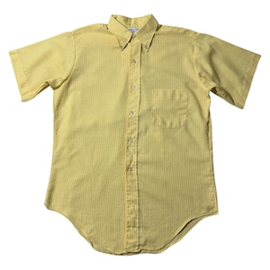 Puede incluir: Camisa amarilla de manga corta con rayas verticales. La camisa tiene cuello abotonado, bolsillo en el pecho y dobladillo curvo. Fabricada en tejido ligero, es adecuada para climas cálidos.