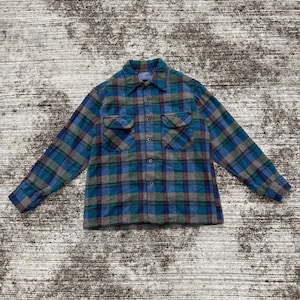 May include: A long-sleeved, button-down shirt with a plaid design. The shirt's colours include teal, blue, grey, and maroon. It has two chest pockets and a standard collar. The shirt is laid flat, displaying its pattern and texture.