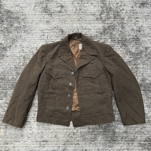 May include: A brown jacket with four front pockets and a button-up closure. The jacket has a notched collar and a tan lining. The jacket appears to be made of a wool or wool-blend fabric. The jacket is vintage and shows signs of wear.