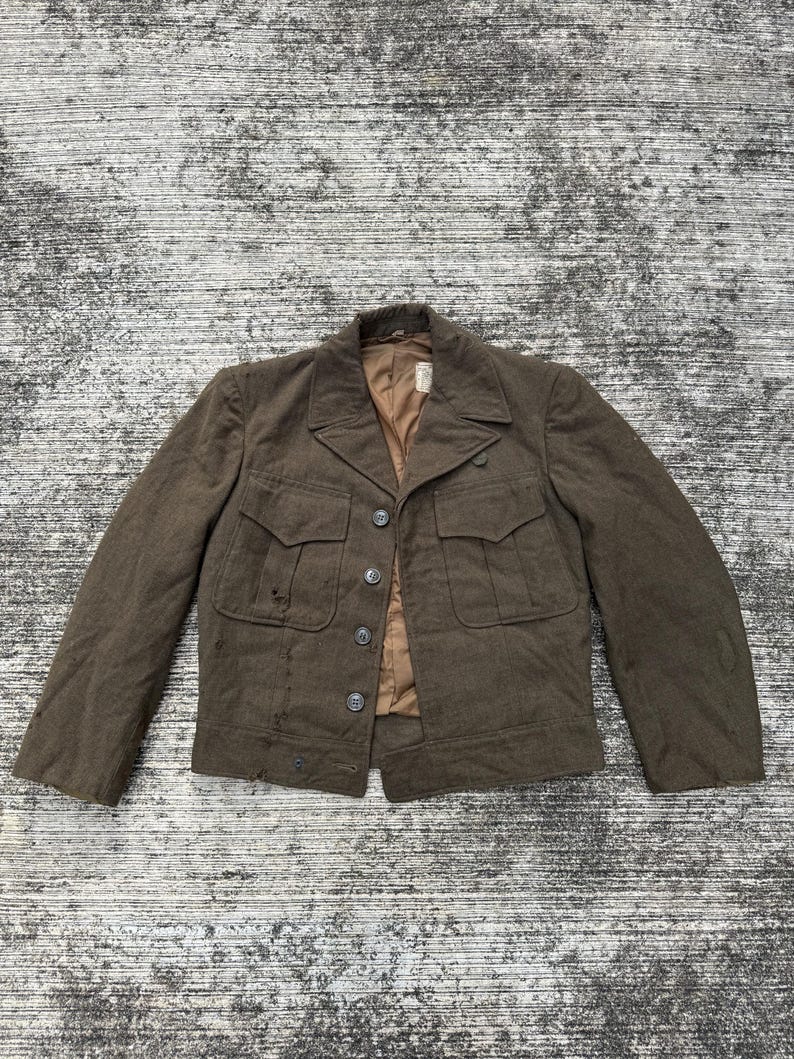 Puede incluir: Chaqueta marr&oacute;n con cuatro bolsillos delanteros y cierre de botones. La chaqueta tiene cuello con solapas y forro beige. La chaqueta parece estar hecha de lana o mezcla de lana. La chaqueta es vintage y muestra signos de desgaste.
