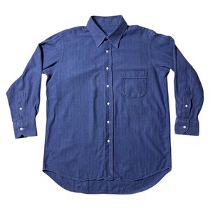 Può includere: Camicia blu navy a maniche lunghe con colletto button-down e taschino sul petto. La camicia ha polsini con bottoni e orlo curvo. Il tessuto è un materiale morbido e tessuto. Stile classico.