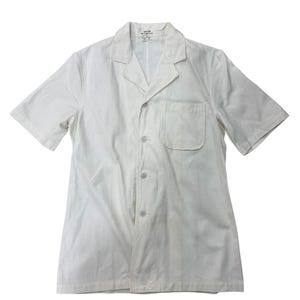 May include: A white, short-sleeved shirt with a single chest pocket and a classic collar. The shirt fastens with buttons and has a relaxed fit. The buttons are a light, neutral colour. The shirt is made of a lightweight fabric.