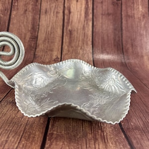 May include: Silver-colored, leaf-shaped serving dish with a decorative spiral handle. The dish has a scalloped edge and embossed floral patterns. A unique piece for serving snacks or small items.