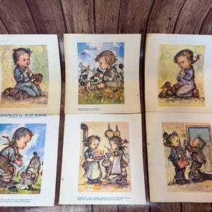 May include: A collection of six vintage prints featuring children in various scenes. The prints, titled "Juveniles by Jean Bukac," depict children with animals and in domestic settings, rendered in soft watercolor hues. The prints are on aged paper.