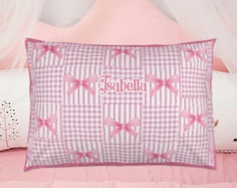 May include: A rectangular pillowcase featuring a patchwork pattern of light pink and white gingham checks and vertical stripes. The design is accented with repeating pink ribbon bows and the name Isabella embroidered in pink script in the center.