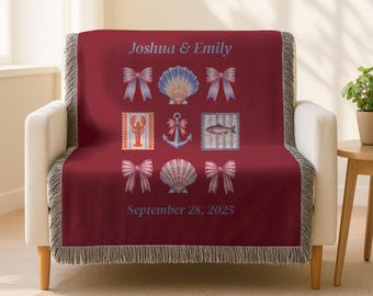 May include: A burgundy throw blanket draped over a white armchair. The blanket features nautical-themed illustrations including bows, seashells, and an anchor. The names "Joshua & Emily" and the date "September 28, 2025" are printed on the blanket.