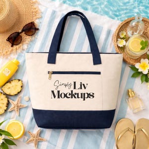 May include: A cream-colored tote bag with navy blue accents, a zippered pocket, and navy blue handles. The bag is on a striped towel with sunglasses, a straw hat, and beach-themed accessories. The text "Simply Liv Mockups" is printed on the bag.