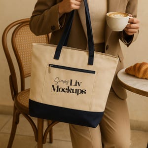 May include: A beige tote bag with navy blue accents, featuring a front pocket with a zipper and the text "Simply Liv Mockups." The bag has navy blue handles. The image also shows a person holding a coffee cup and wearing a brown suit.