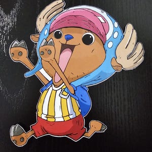 May include: A colorful cartoon sticker of a reindeer-like character with large eyes and a cheerful expression. The character wears a blue hat, a pink cap, a striped yellow and white shirt, and red shorts. The sticker is on a black background.