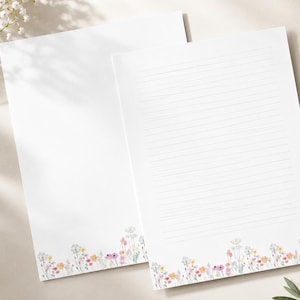 K&ouml;nnte beinhalten: Zwei Blatt wei&szlig;es Briefpapier mit einer zarten Aquarellillustration von Wildblumen in Rosa-, Gelb- und Gr&uuml;nt&ouml;nen am unteren Rand. Ein Blatt ist unbeschrieben, w&auml;hrend das andere feine, horizontale graue Linien zum Schreiben aufweist.