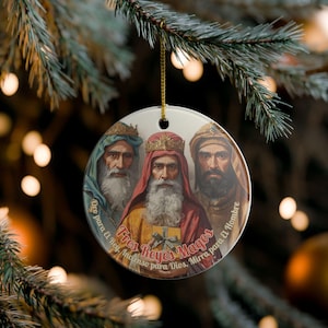 May include: A round Christmas ornament featuring an illustration of the Three Wise Men. The men are depicted with long white beards and wearing crowns and robes in shades of blue, red, and tan. Text in Spanish encircles the image.