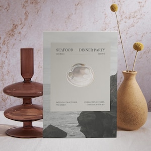 Könnte beinhalten: Eine Einladung zu einem Meeresfrüchte-Dinner mit einer Muschel-Illustration. Die Einladung enthält den Text "SEAFOOD DINNER PARTY" und Veranstaltungsdetails. Ein brauner Glas-Kerzenhalter und eine kleine Vase mit gelben Blumen sind ebenfalls im Bild.