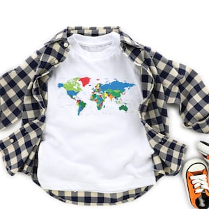 May include: White t-shirt with a colorful world map graphic, layered under a navy and cream plaid button-down shirt. The text "White" is at the bottom of the image. Orange and white sneakers are visible.