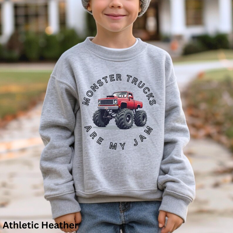 Puede incluir: Sudadera gris jaspeado con un gr&aacute;fico circular que presenta un cami&oacute;n monstruo rojo y el texto "MONSTER TRUCKS ARE MY JAM". La sudadera est&aacute; hecha de un material suave.
