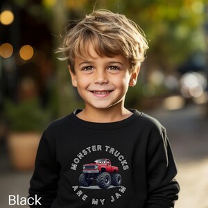 Puede incluir: Sudadera negra con un dise&ntilde;o de cami&oacute;n monstruo rojo y el texto "MONSTER TRUCKS ARE MY JAM". La sudadera la lleva un ni&ntilde;o peque&ntilde;o. El fondo est&aacute; borroso con tonos verdes y amarillos.