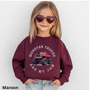 Puede incluir: Sudadera granate con un gr&aacute;fico de cami&oacute;n monstruo rojo y el texto "MONSTER TRUCKS ARE MY JAM". La sudadera es usada por un ni&ntilde;o que lleva gafas de sol en forma de coraz&oacute;n.
