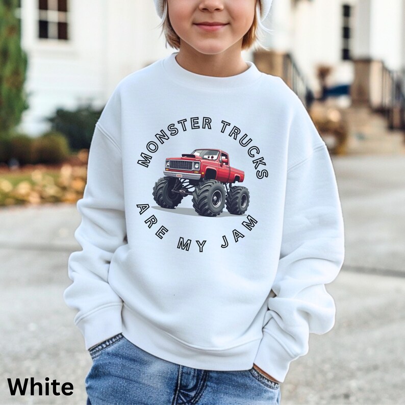Puede incluir: Sudadera blanca con un gr&aacute;fico de cami&oacute;n monstruo rojo y el texto "MONSTER TRUCKS ARE MY JAM". La sudadera la lleva un ni&ntilde;o y se combina con vaqueros azules.