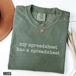 Op de afbeelding: Een mosgroen t-shirt met korte mouwen, een ronde hals en de witte tekst "my spreadsheet has a spreadsheet" op de voorzijde. Het shirt is voorzien van een Comfort Colors merklabel in de nek en een kleine gouden ketting met hanger.