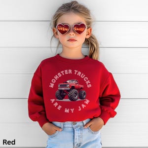 Puede incluir: Una sudadera roja con el texto blanco "MONSTER TRUCKS ARE MY JAM". El gr&aacute;fico presenta un cami&oacute;n monstruo rojo con grandes neum&aacute;ticos negros. La sudadera la lleva un ni&ntilde;o.