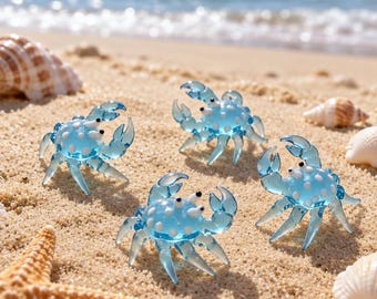 May include: Four small, translucent light blue glass crab figurines, each featuring white polka dot patterns on their shells and raised claws. The crabs have tiny black eyes and are positioned on a sandy surface with various seashells.