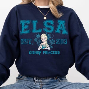 A navy blue sweatshirt with a graphic design featuring the character Elsa from the Disney movie Frozen.